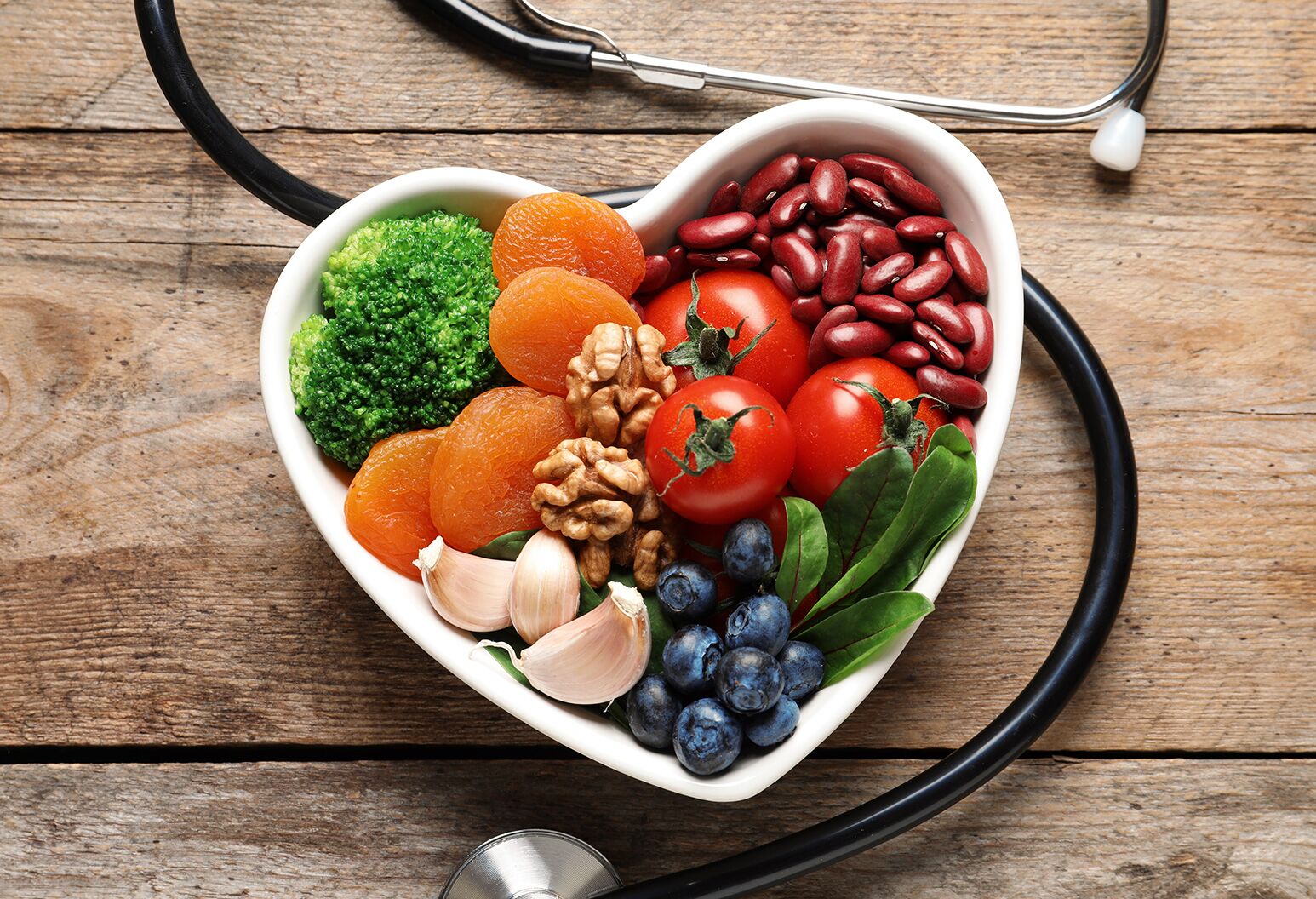 Heart-shaped bowl filled with fruits and vegetables surrounded by a stethoscope.