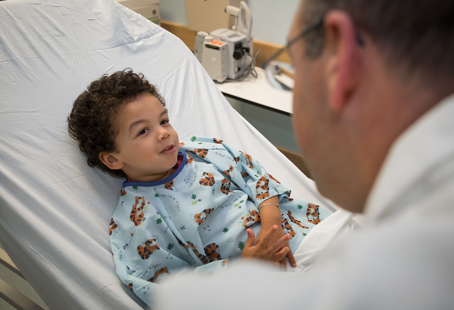 A child lays in a hospital bed and looks up at a provider.