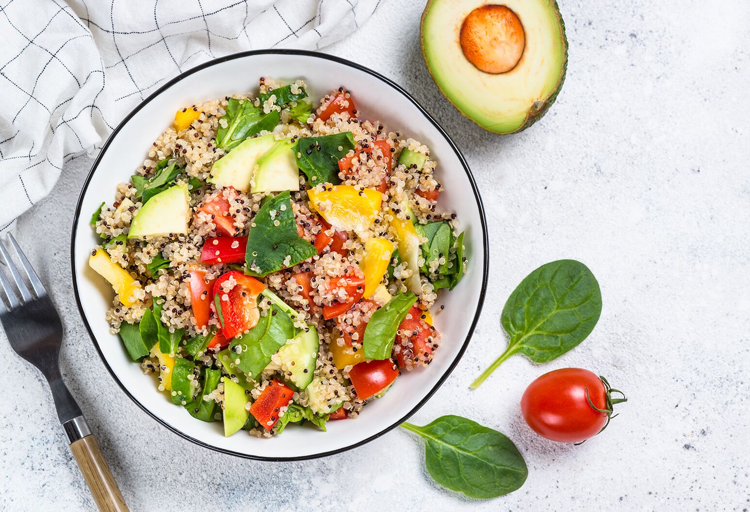 A bowl of quinoa and veggies with a cut avocado and tomato.