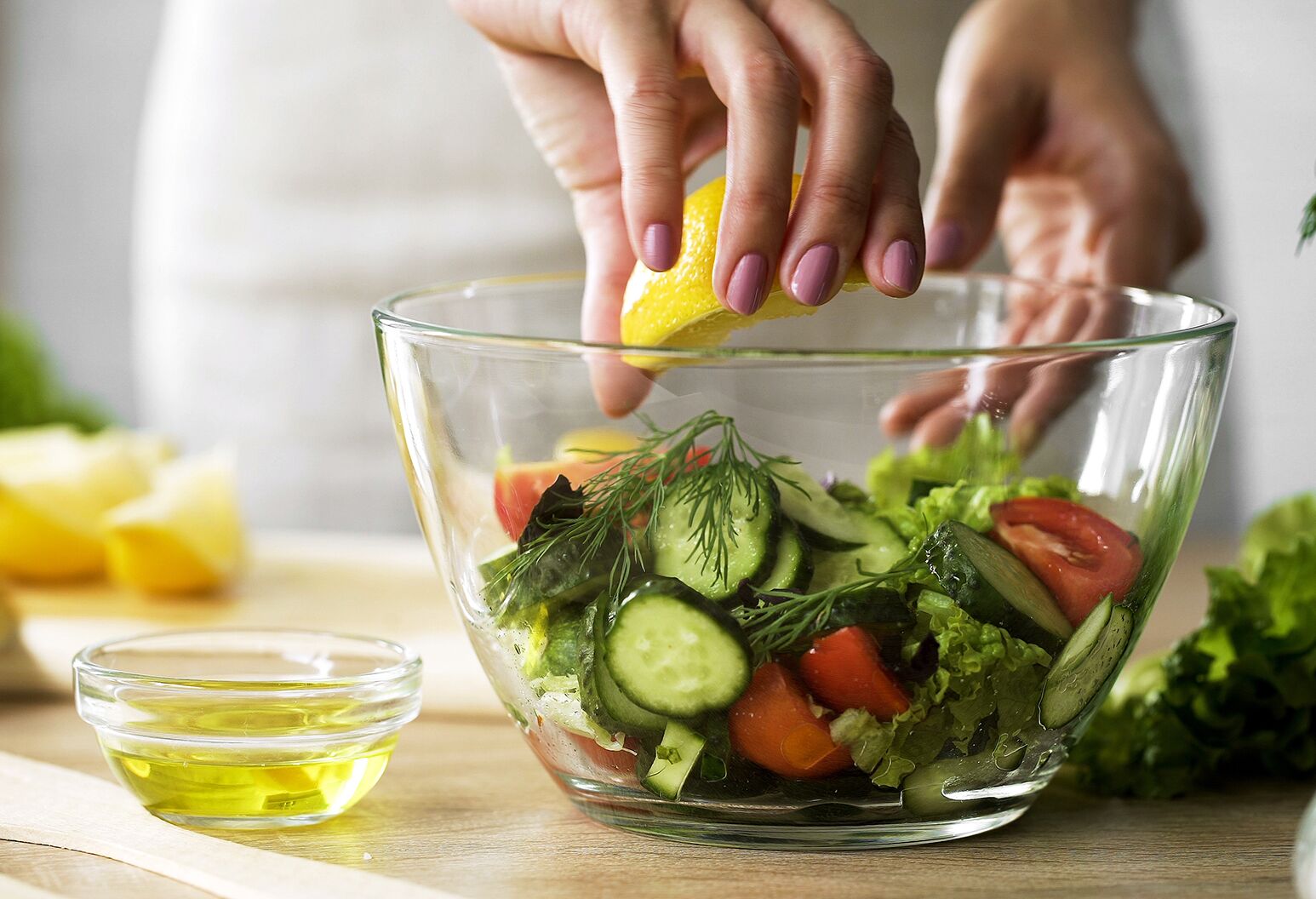 A person squeezing lemon into a bowl of vegetables.