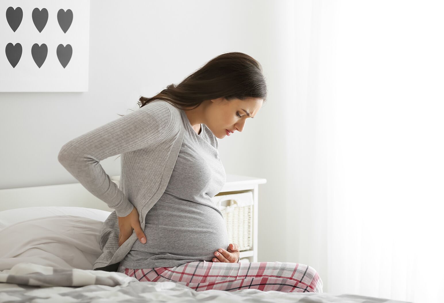 A pregnant woman sitting up in bed, holding her back in pain.