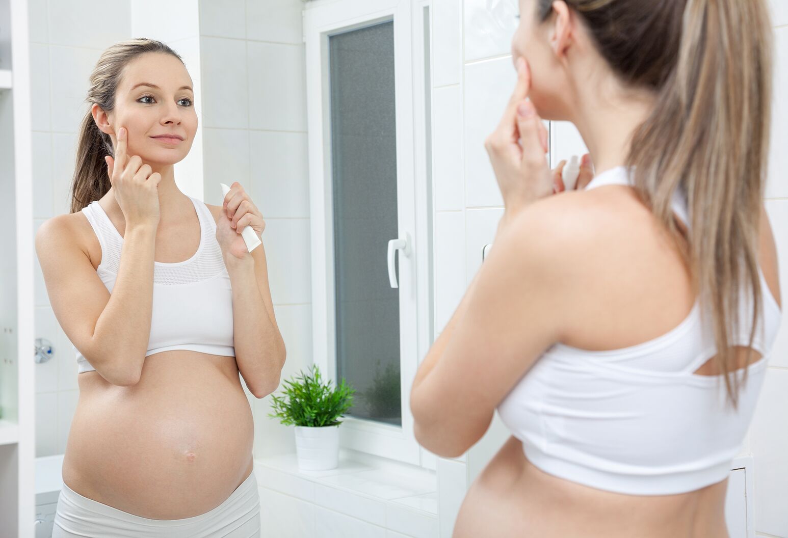 A pregnant woman putting lotion on her face.
