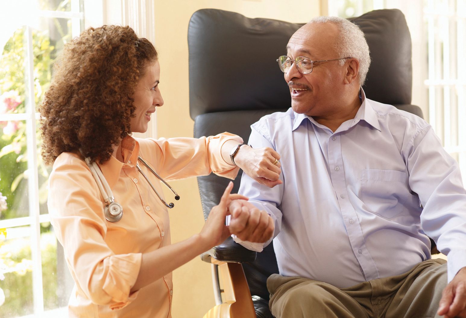 female physician smiling while checking pulse of elderly man sitting in chair
