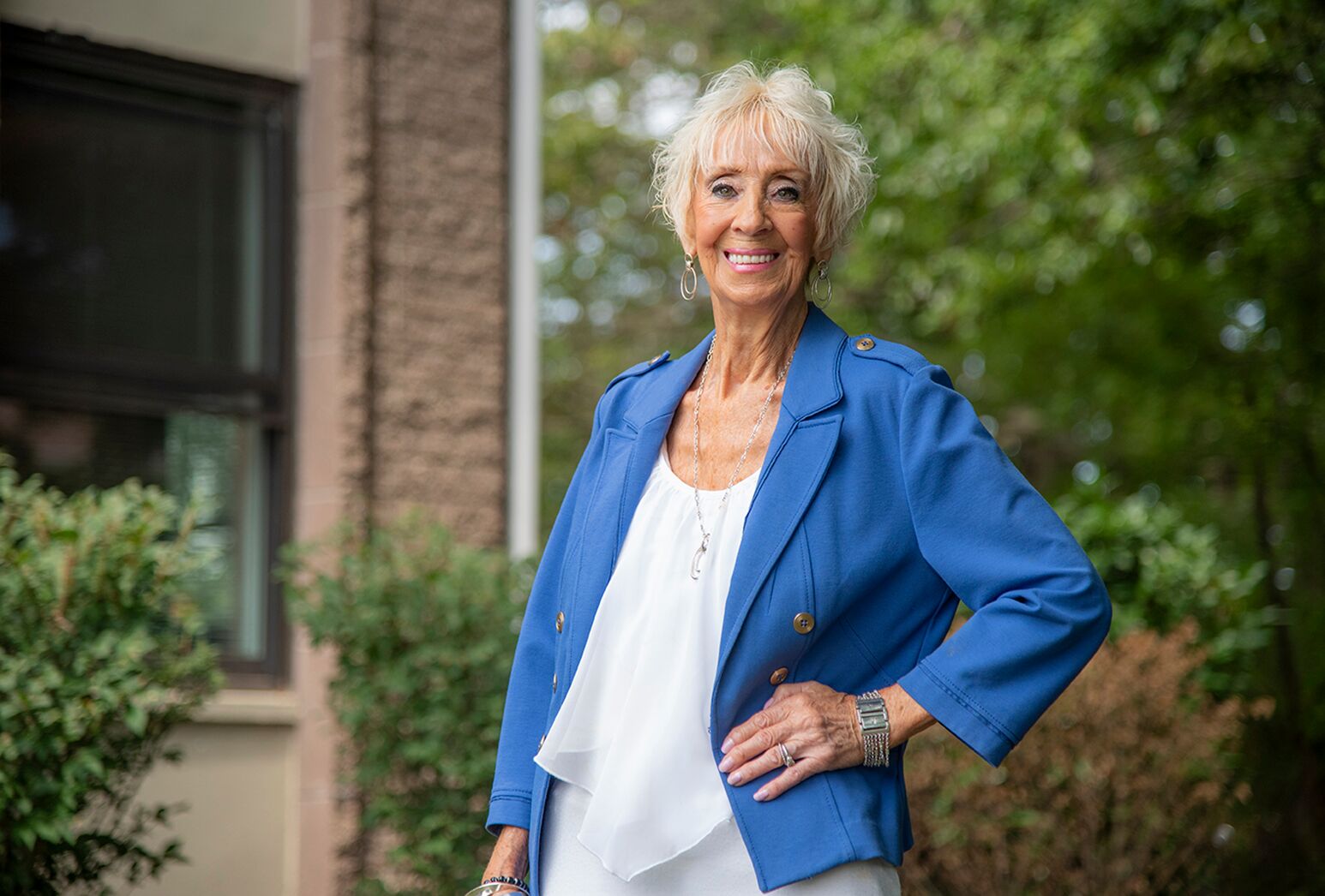 Woman with cropped gray hair, a white top and a blue jacket, standing outside