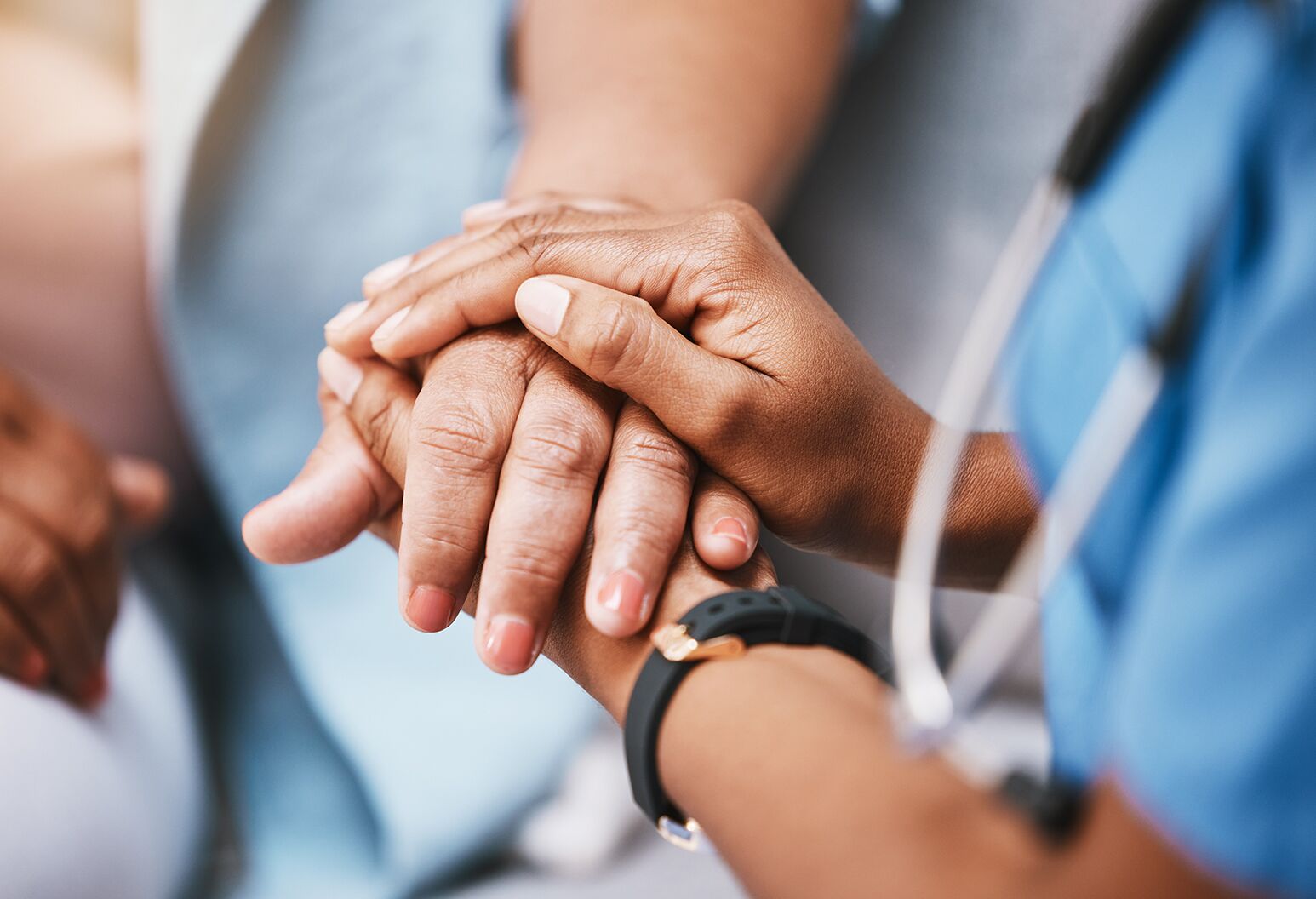 A nurse clasps the hands of a patient in a light blue hospital gown at left.