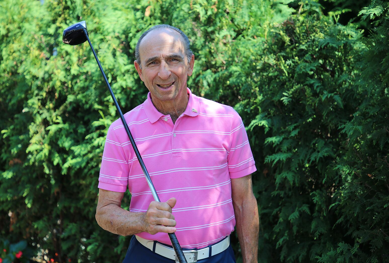 Older man treated for prostate cancer wearing a pink striped shirt holding a golf club.