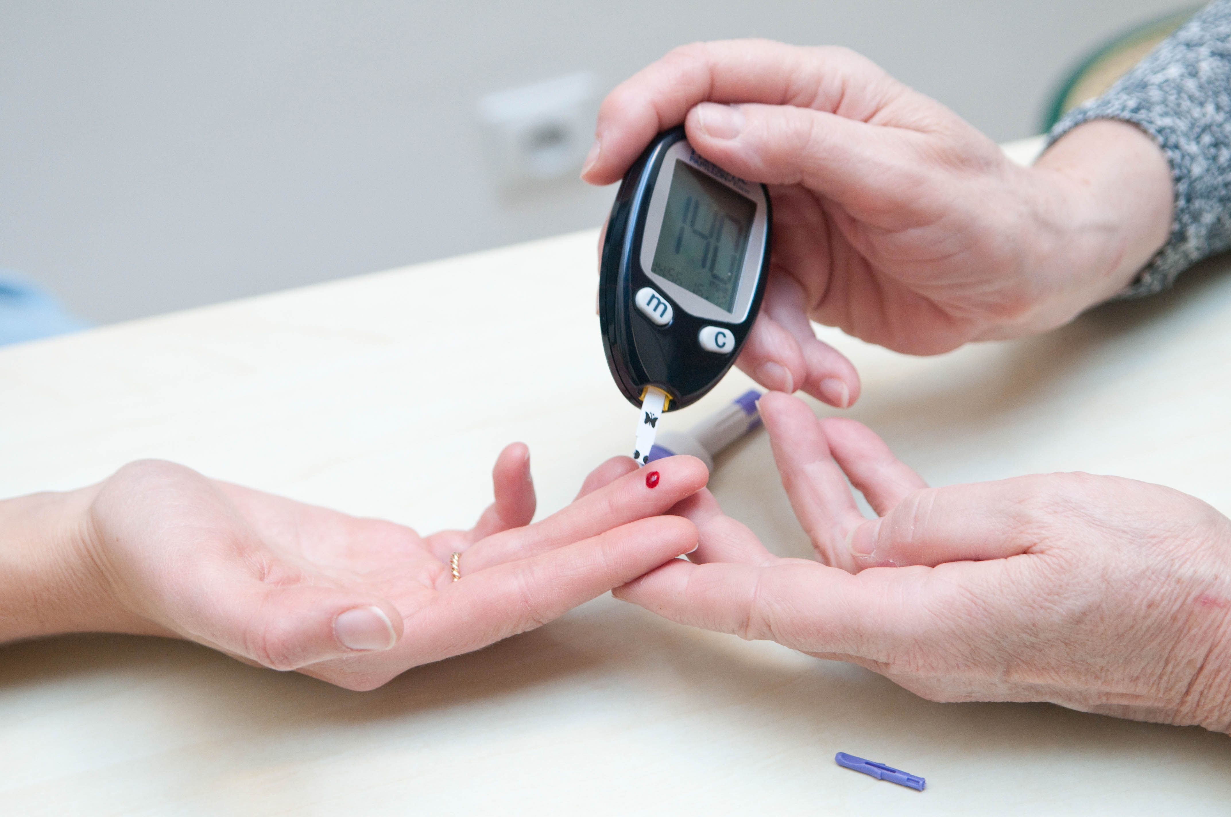 A person administers a blood sugar test to another person using his or her finger.
