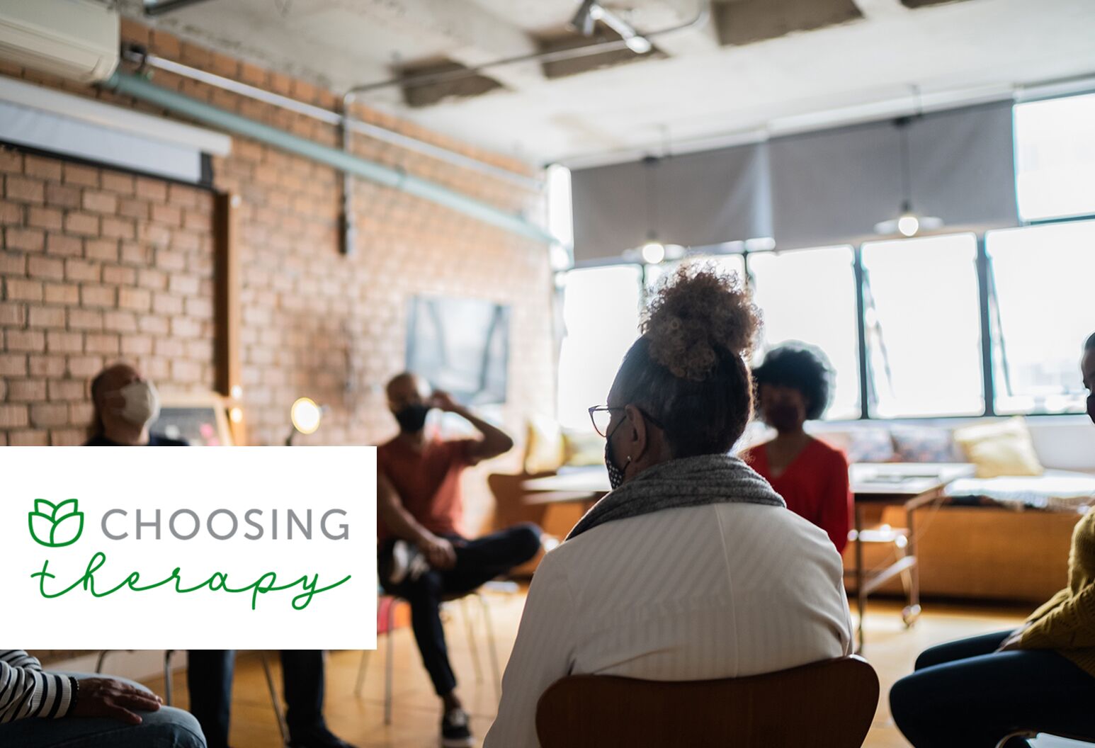 Obscured image of a group of people sitting in a therapy session in a large, open brick space.