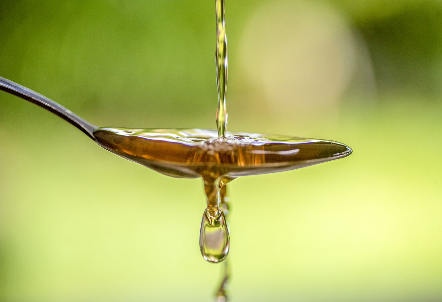 Micro shot of apple cider vinegar being poured over spoon in front of green background.