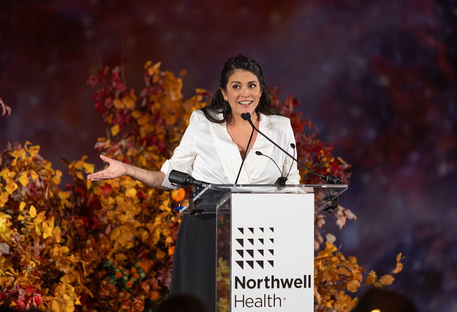 A woman in a white jacket stands at a Northwell Health-branded podium and speaks.