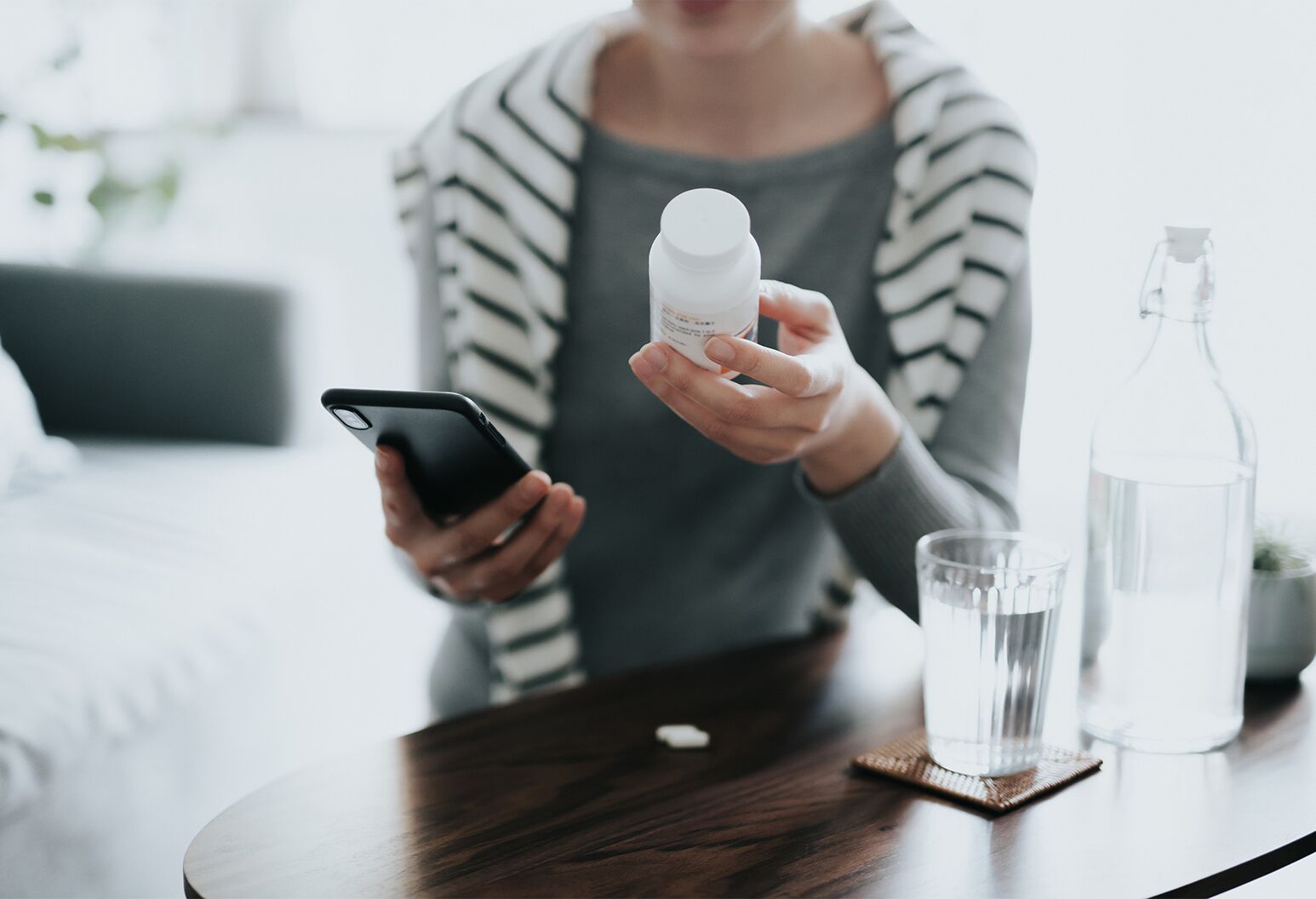 Close up image of a young woman holding a cell phone in one hand and a pill bottle in the other.