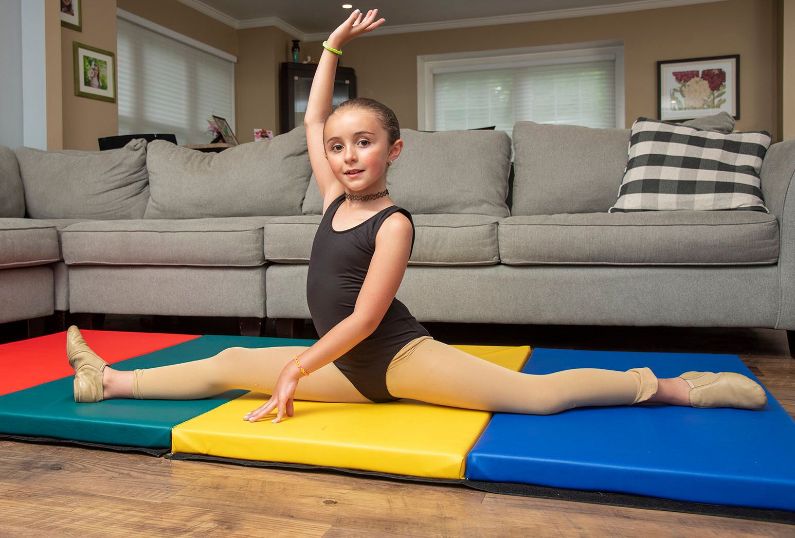 Young girl in black leotard doing a split on a gymnastics mat in her home.