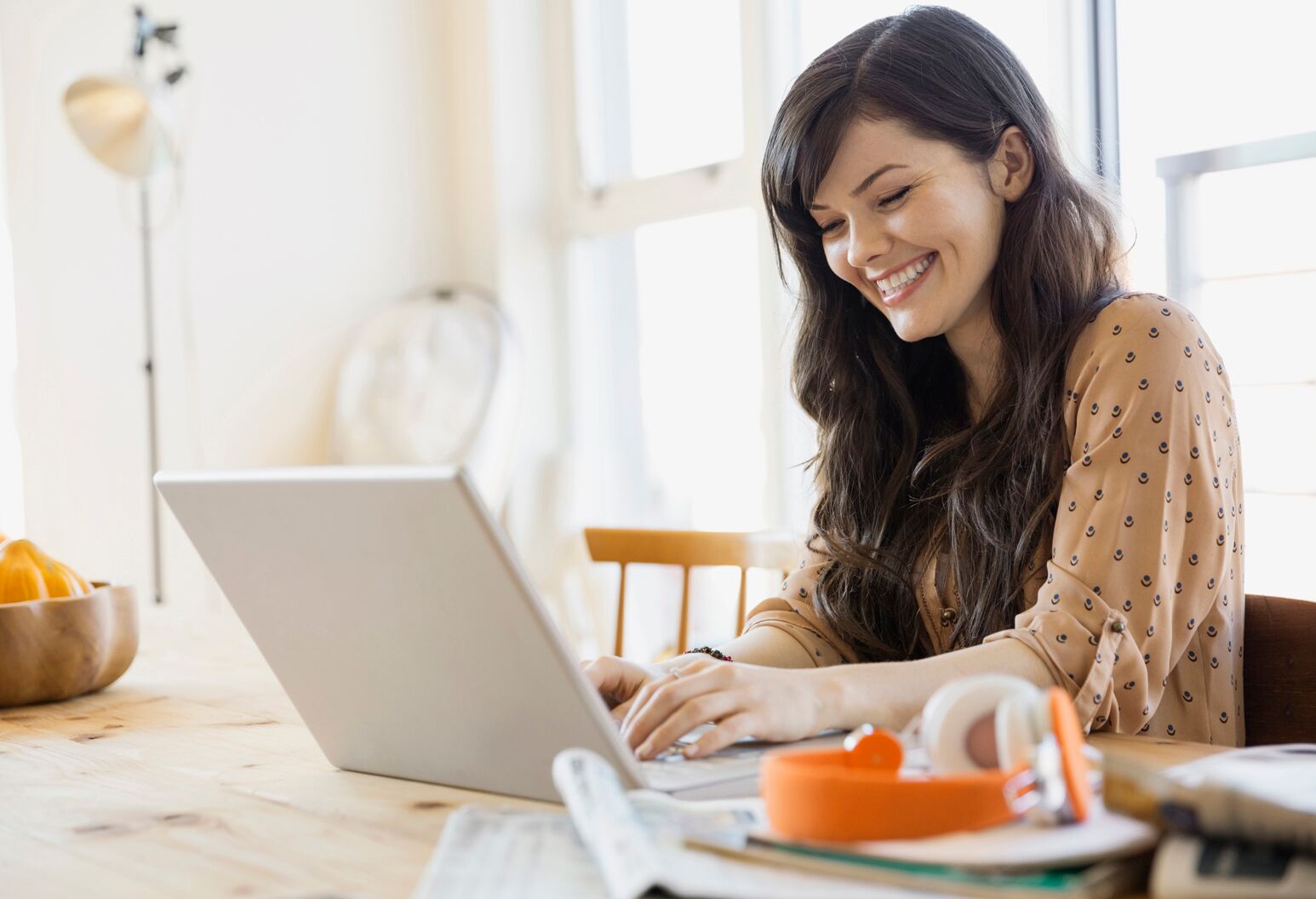 A smiling woman sits at table using her laptop.