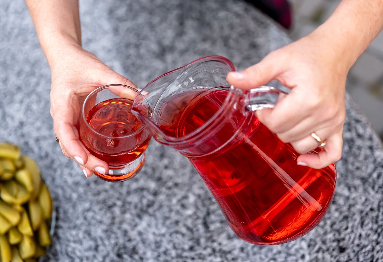 A woman pouring cranberry juice from a glass pitcher into a drinking glass.