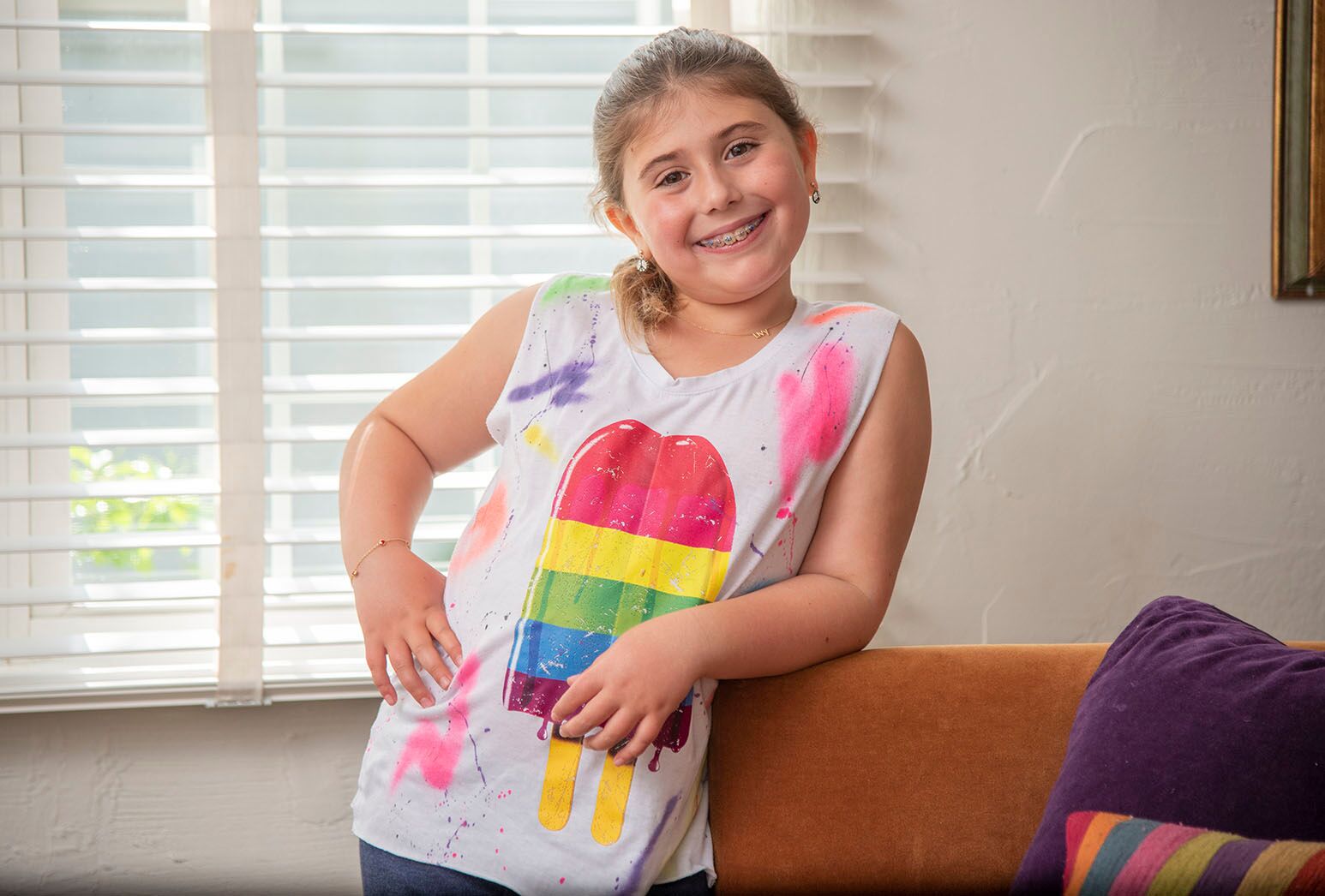 Young girl with a bright ice cream pop on her shirt smiling in her home.