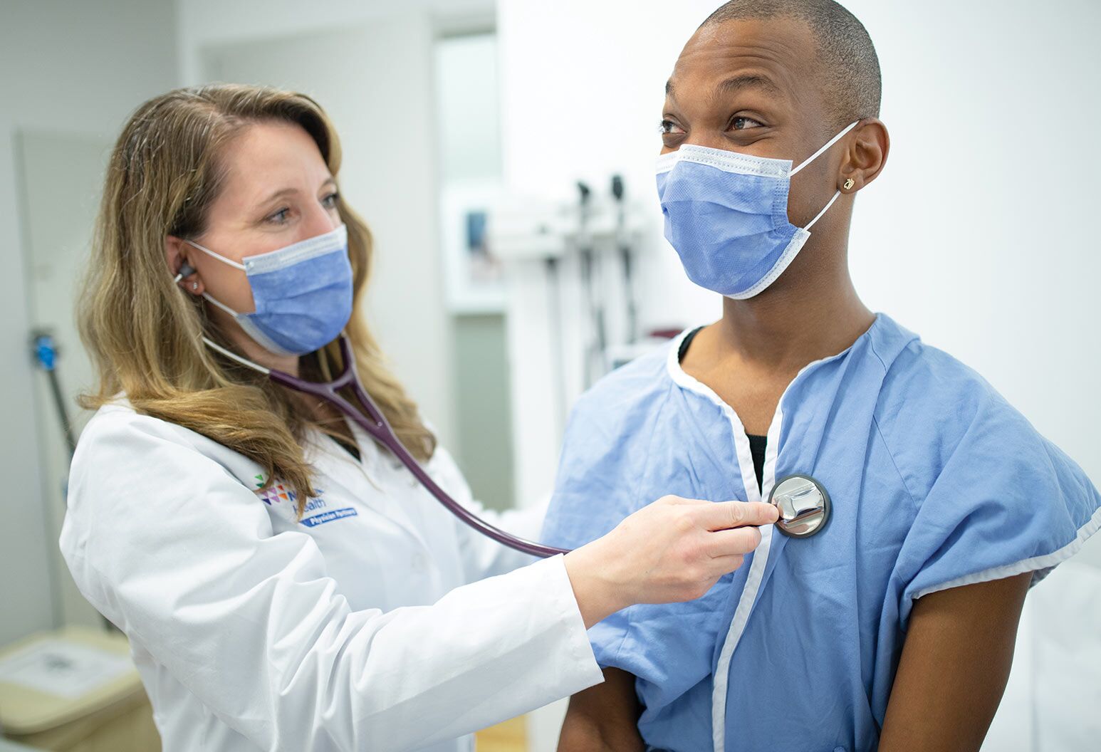 A doctor in a mask uses a stethoscope on a patient in a mask.