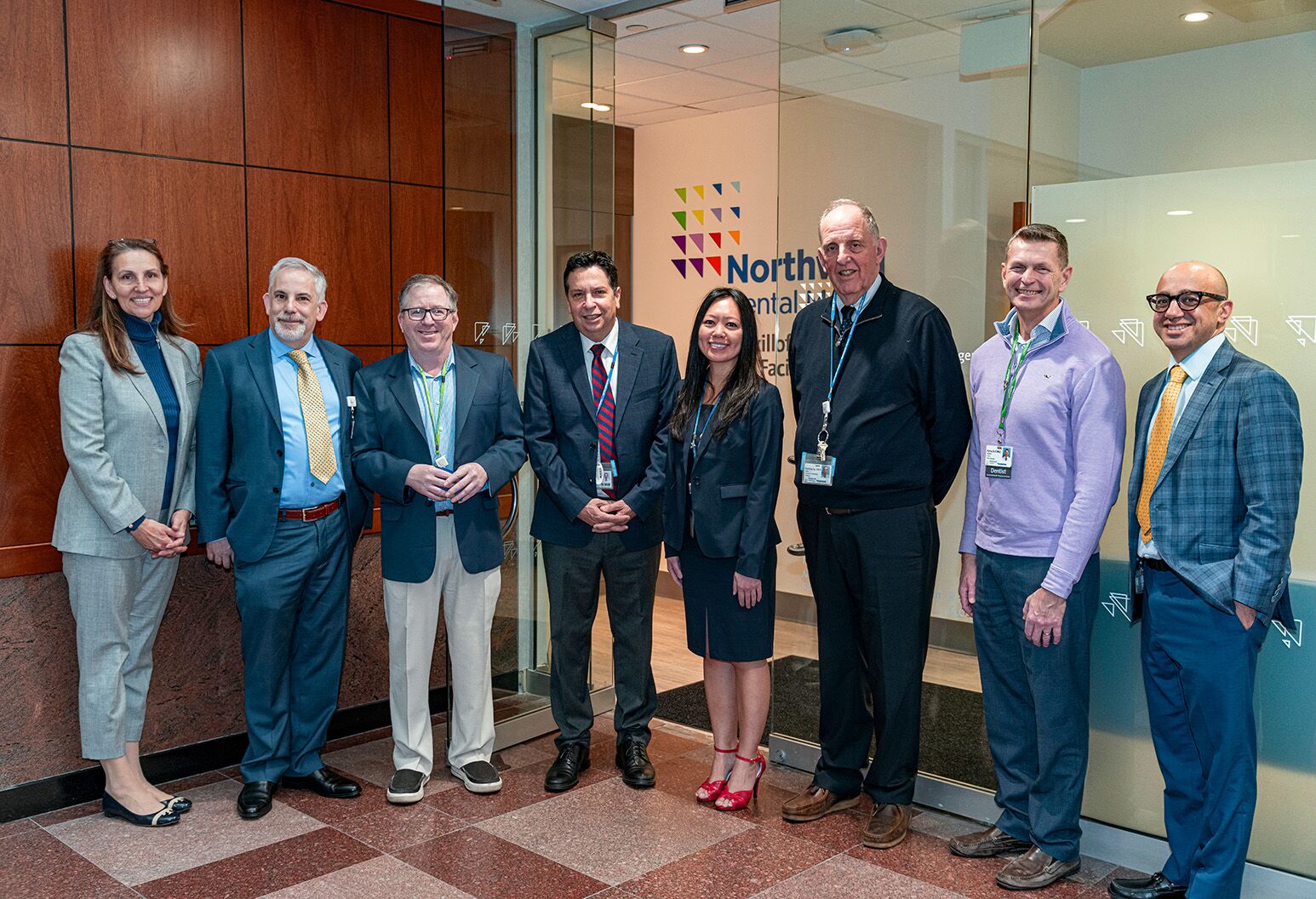 Several men and women in professional dress stand in a line against a Northwell backdrop and pose for a photograph.