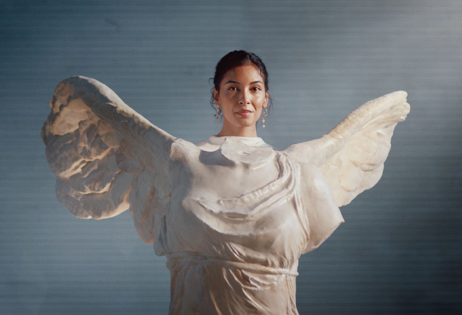 A woman stands behind a statue of angel wings, creating the illusion that she has wings.