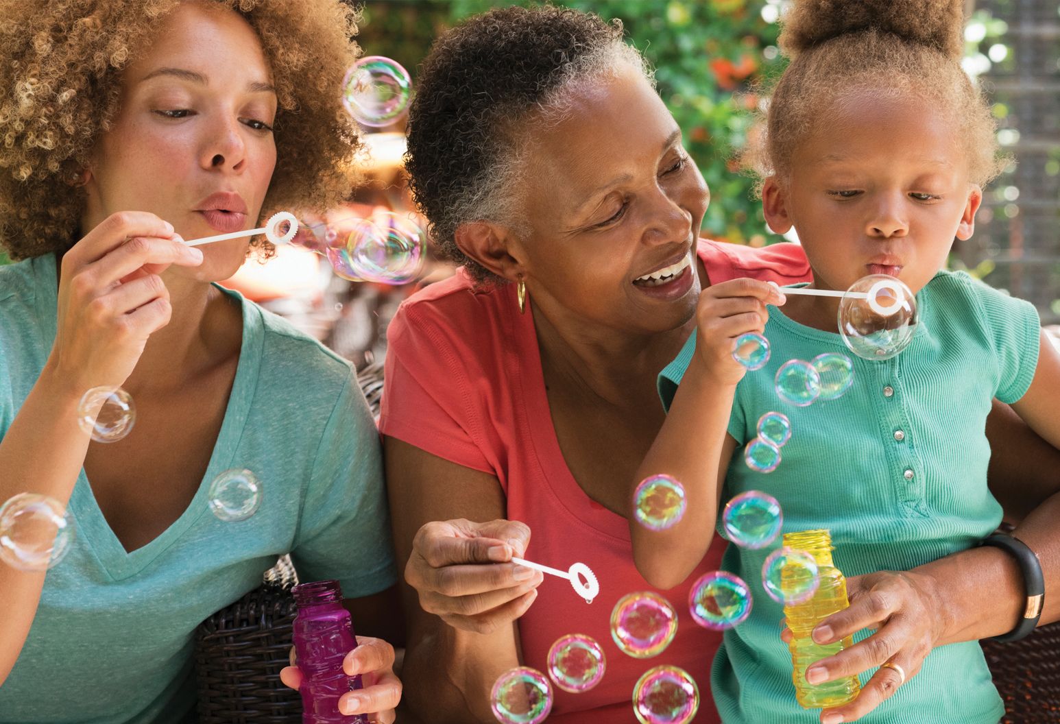 Women of three different generations blowing bubbles outside.