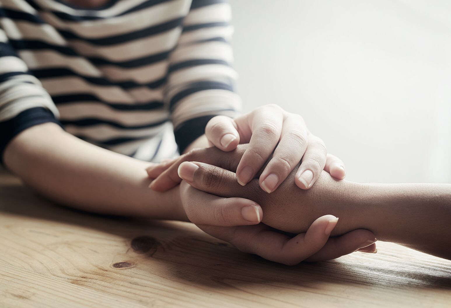 Clasped hands with female in striped shirt in background