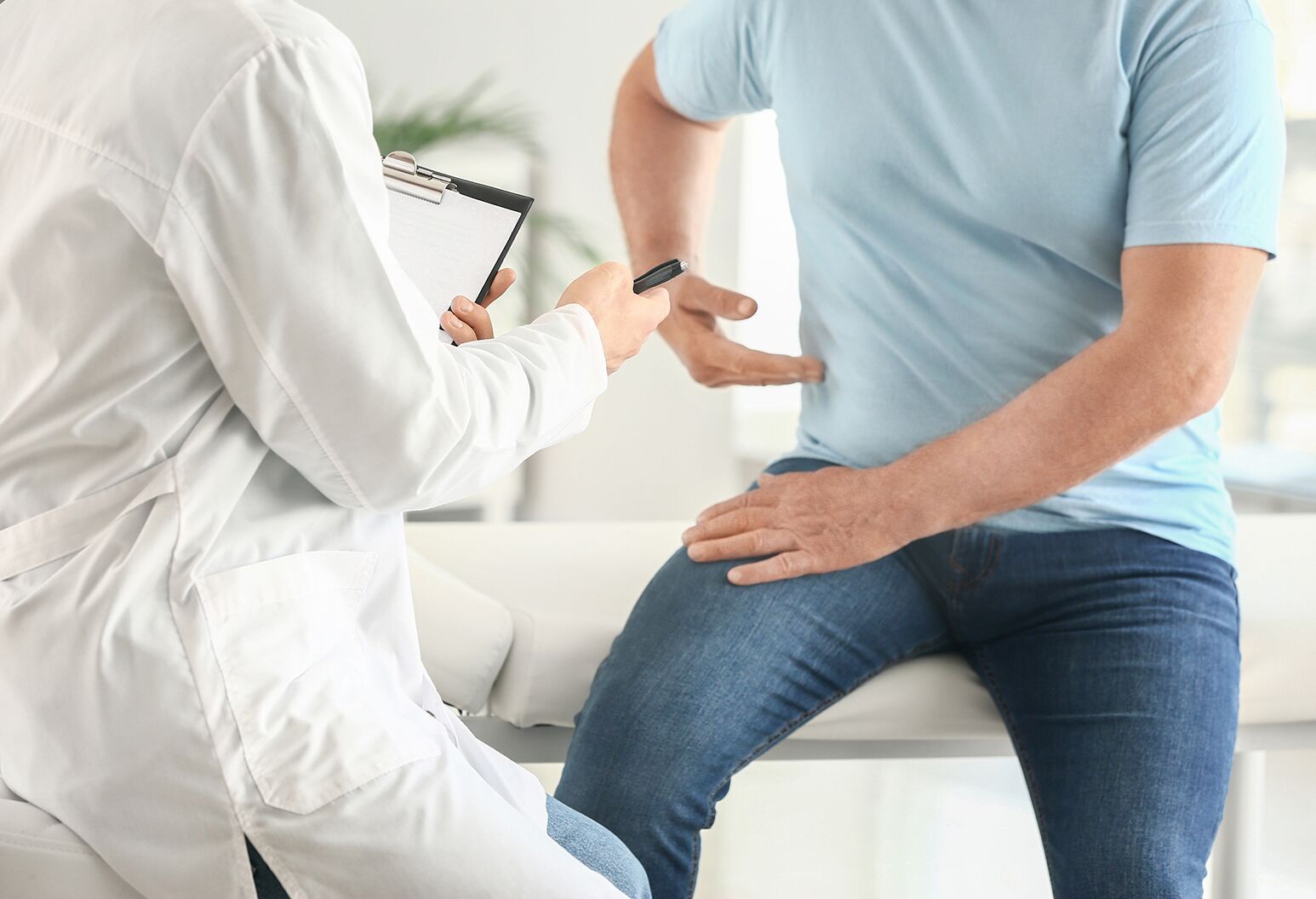 Patient sitting on exam table and pointing to his sides while consulting with a doctor.