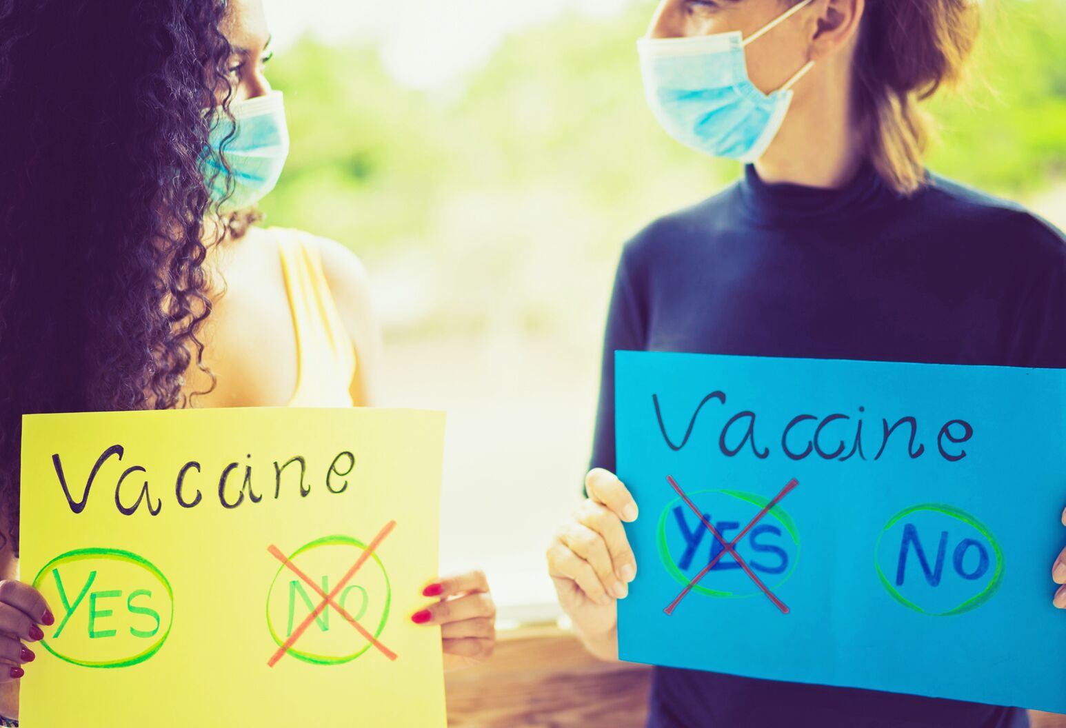 Two women hold conflicting signs about getting vaccinated, which Mark Jarrett, MD, says is critical to avoiding another outbreak of infectious disease like COVID-19.