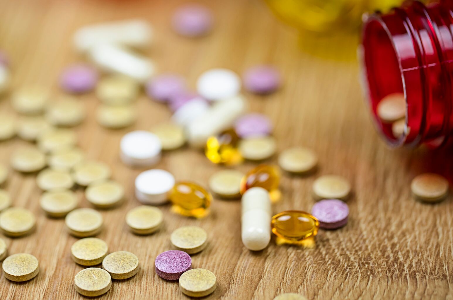 Various different types of pill capsules lay scattered on a wooden table.
