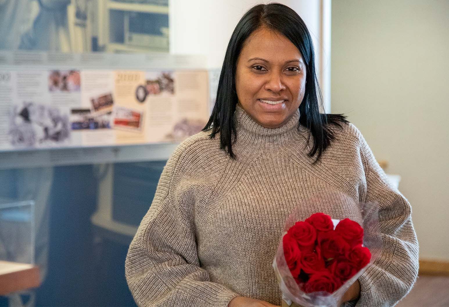 Woman with dark hair wearing a gray turtleneck holds bouquet of red roses.
