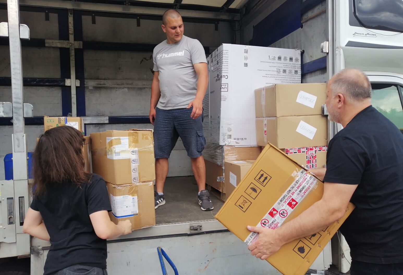 Three people unload boxes from a truck. 