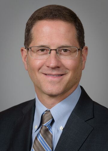 Jeffrey Kuvin, MD, wearing a dark suit, blue shirt and gray and blue tie